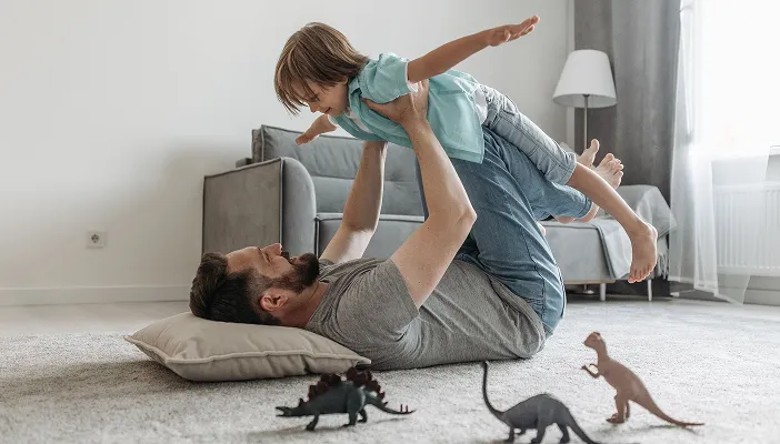 A father playing aeroplane with his son in the living room